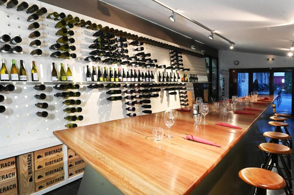 Barra de cata en una bodega del Languedoc-Rosellón, con una pared de botellas sujetas en soportes metálicos al fondo